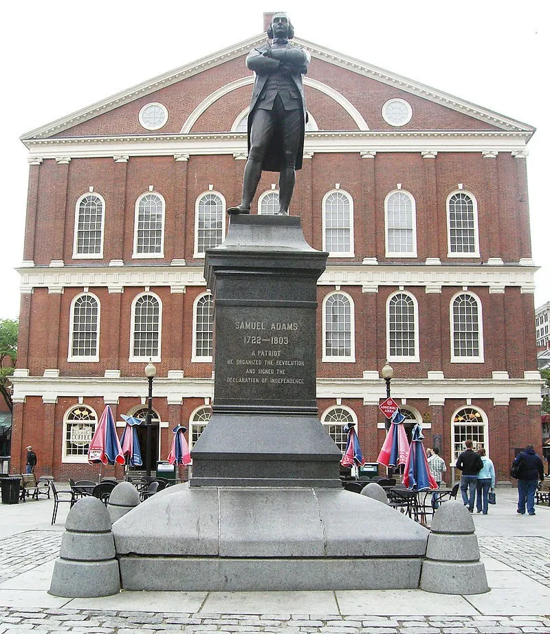 Statue of Samuel Adams in front of Faneuil Hall, Boston, with pedestrians nearby.