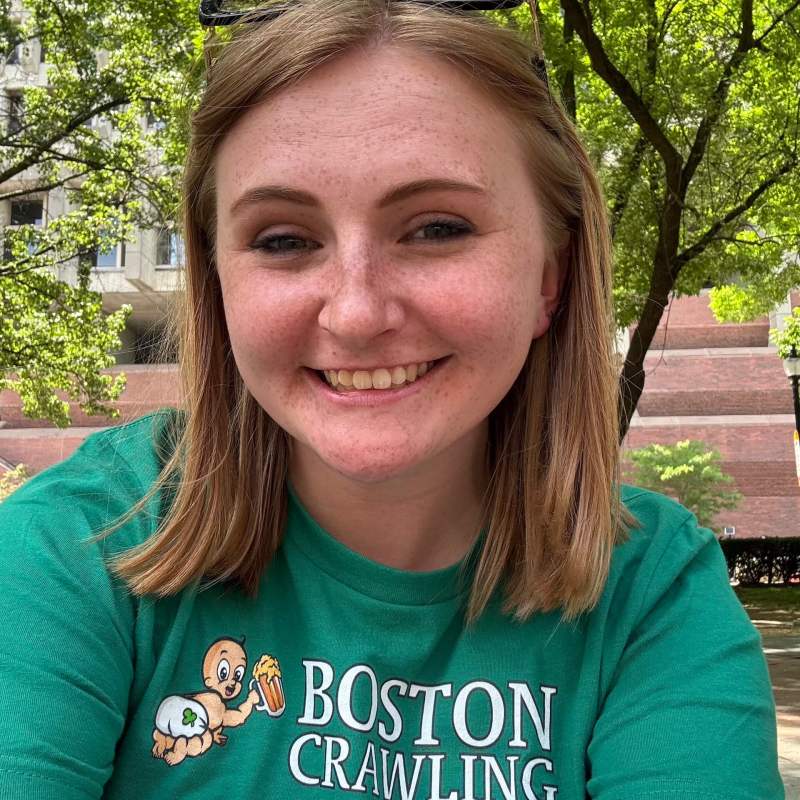 Smiling person in green 'Boston Crawling' t-shirt, outdoors with trees in background.